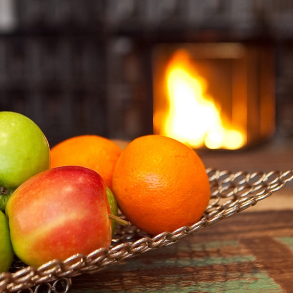 Obstschale mit Äpfeln und Orangen vor dem Kamin