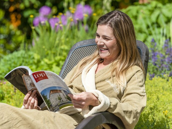 Frau entspannt auf einer Sonnenliege und liest in einem Magazin